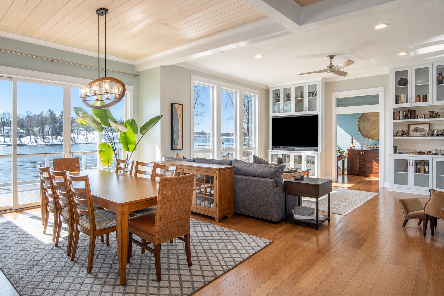 Open-plan sunroom conversion with large windows overlooking a snowy waterfront, dining table, sofa, and built-in shelving.