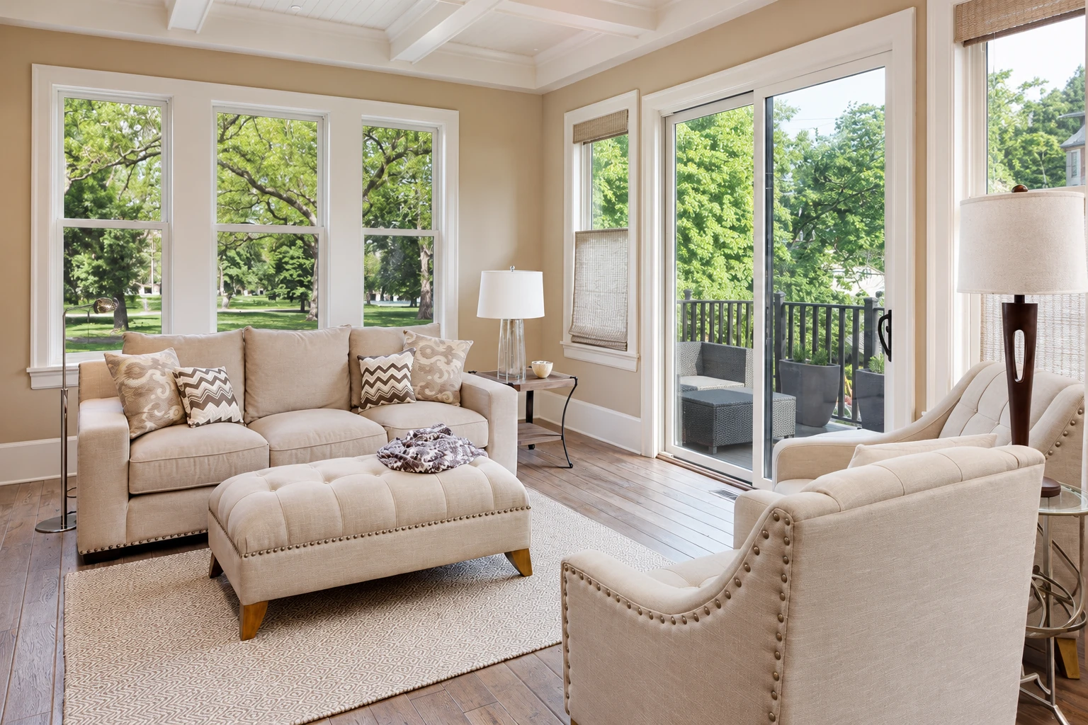 A neutral-toned sunroom with large windows and sliding glass doors opens onto a deck, furnished with sofas and chairs.