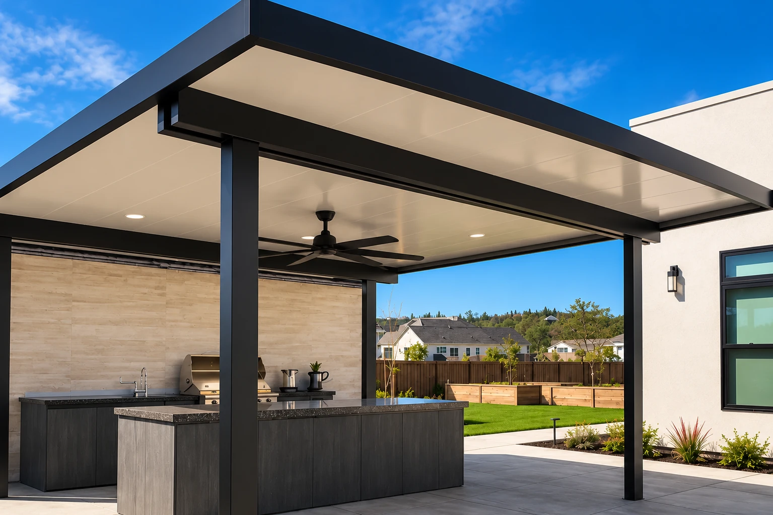 Covered patio with a modern black-framed roof, ceiling fan and outdoor kitchen beside a landscaped yard.