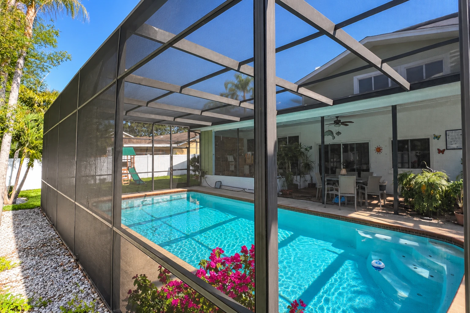 Screen room enclosure surrounds a backyard swimming pool, with dark mesh panels and a screened roof.