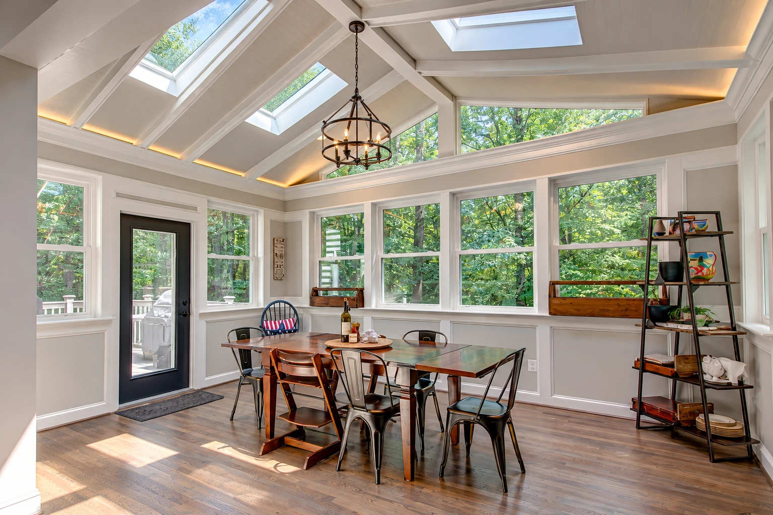 Bright sunroom dining area with a vaulted skylight ceiling, chandelier, large windows, and a wooden table surrounded by mixed chairs.